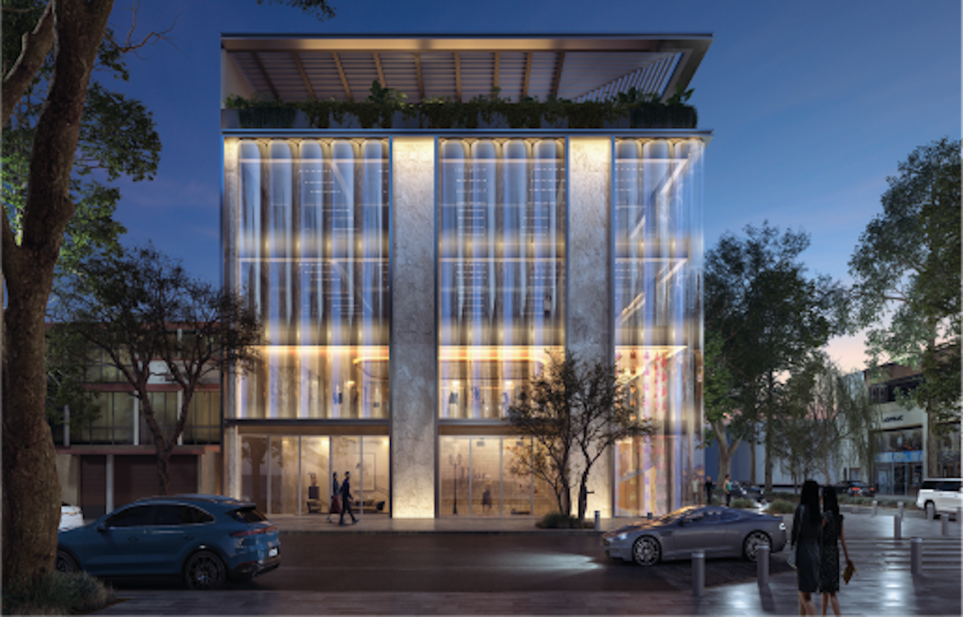 Edificio moderno de uso mixto iluminado por la noche, destacando su fachada de vidrio y estructura vertical. Espacios comerciales visibles en la planta baja, con un diseño que integra elementos naturales.