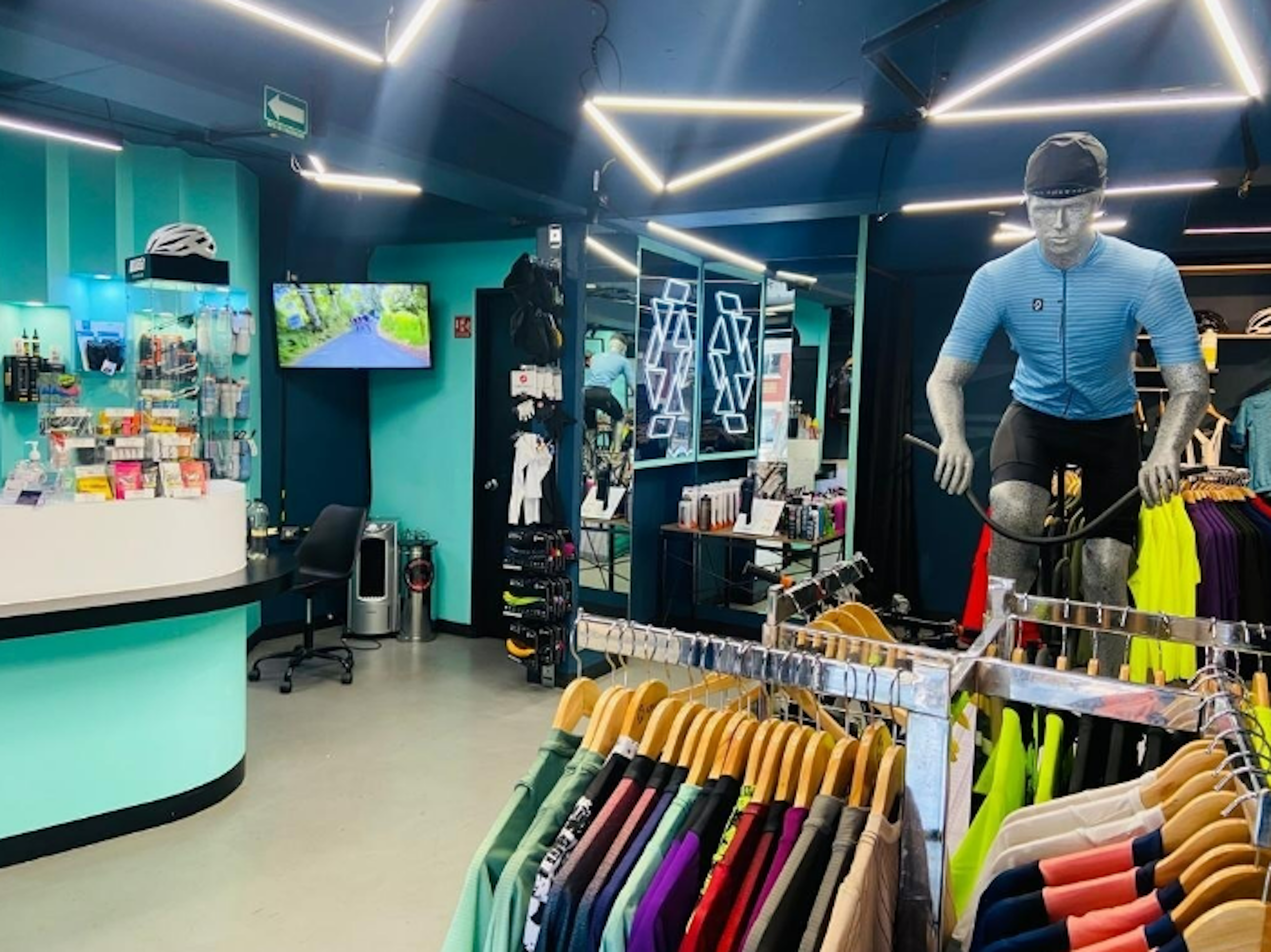 Interior de tienda de ciclismo moderna con iluminación LED, mostradores de atención, maniquí con ropa de ciclista y estantes con productos variados.