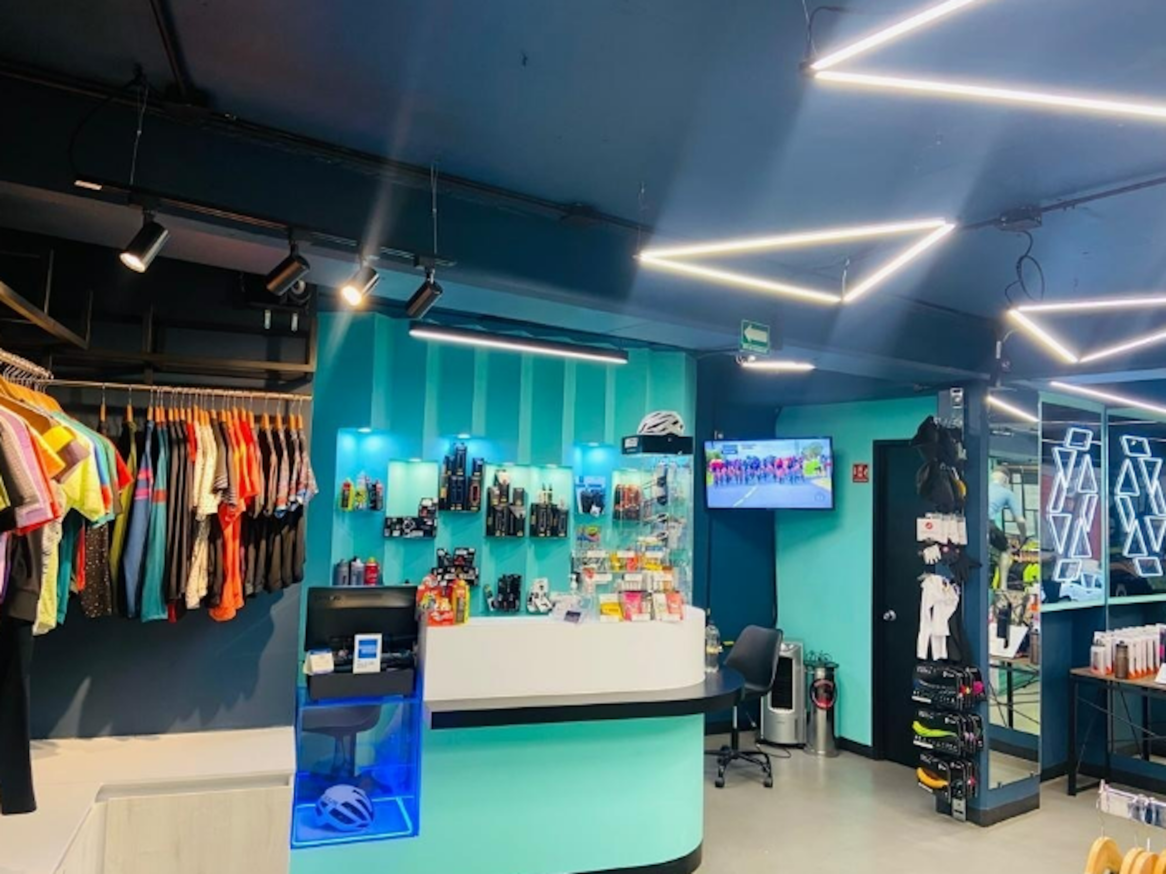 Interior moderno de una tienda con iluminación LED y mobiliario contemporáneo. Exhibición de ropa y accesorios deportivos con mostrador de atención al cliente.