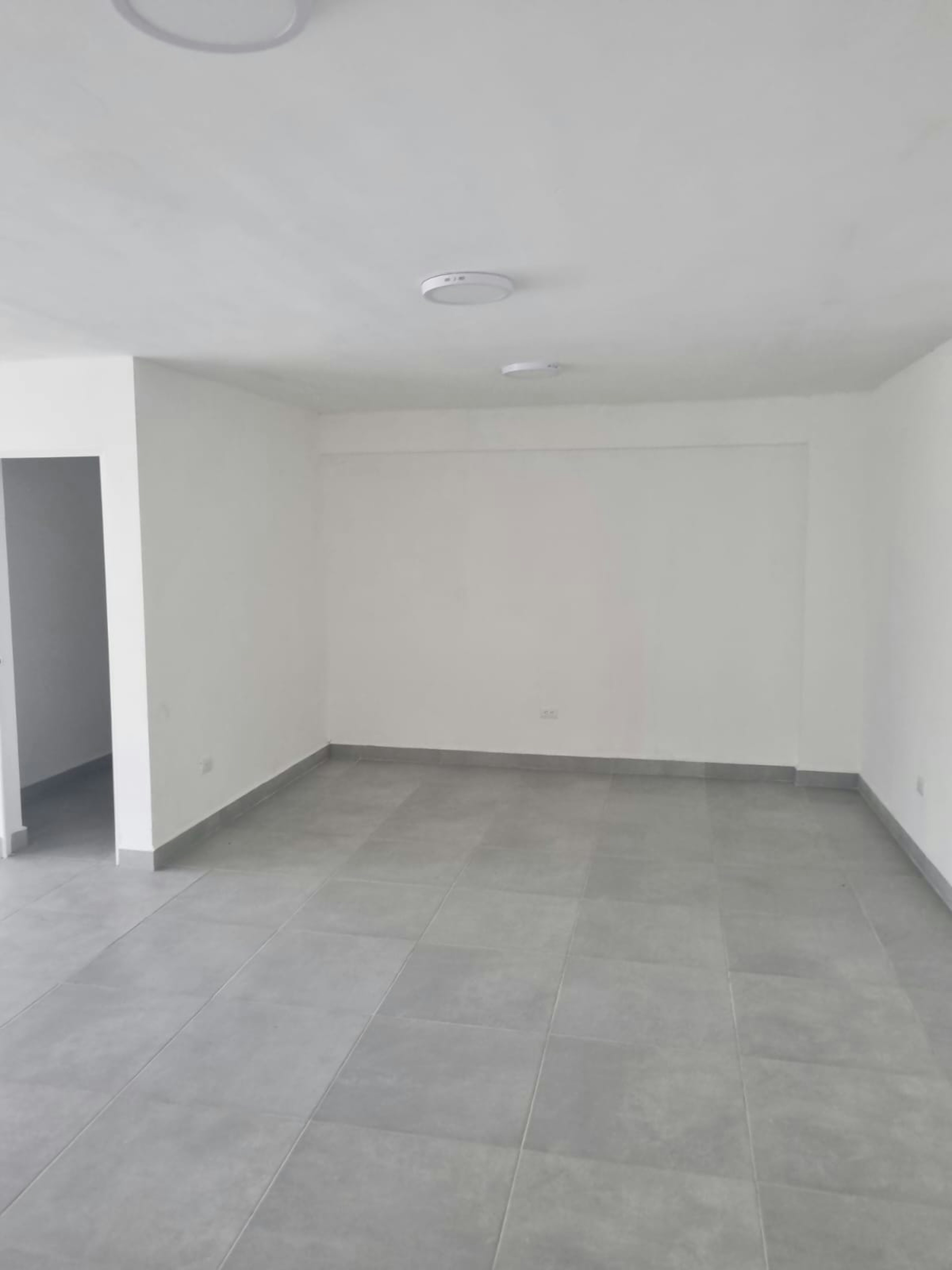 Espacioso interior de propiedad inmobiliaria, con pisos de baldosas grises, paredes blancas y buena iluminación. Ideal para personalizar y adaptar a diversas necesidades residenciales o comerciales.