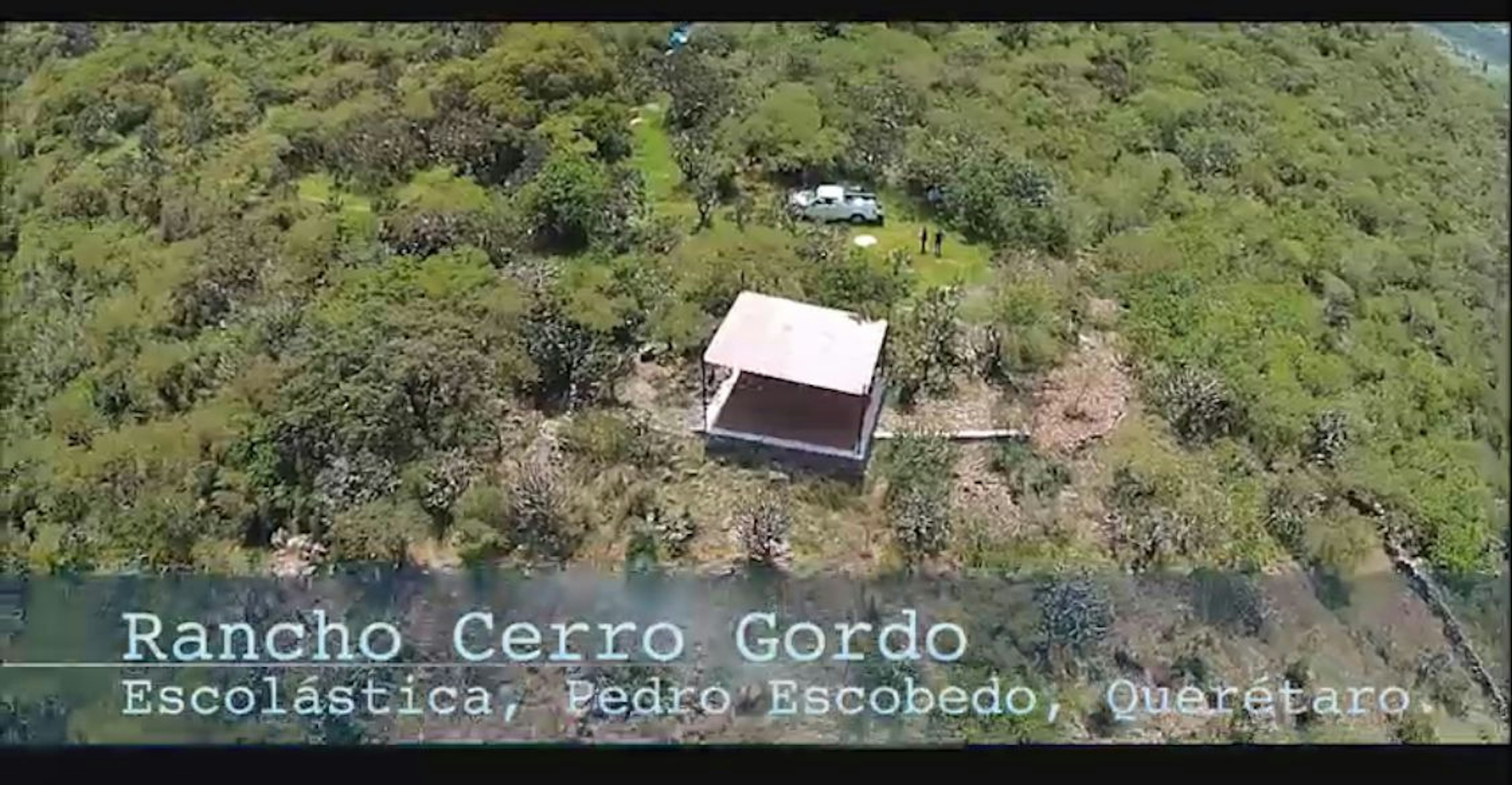 Vista aérea de un rancho ubicado en una zona rural con vegetación densa. Se observa una estructura con techo a dos aguas y un vehículo cercano.