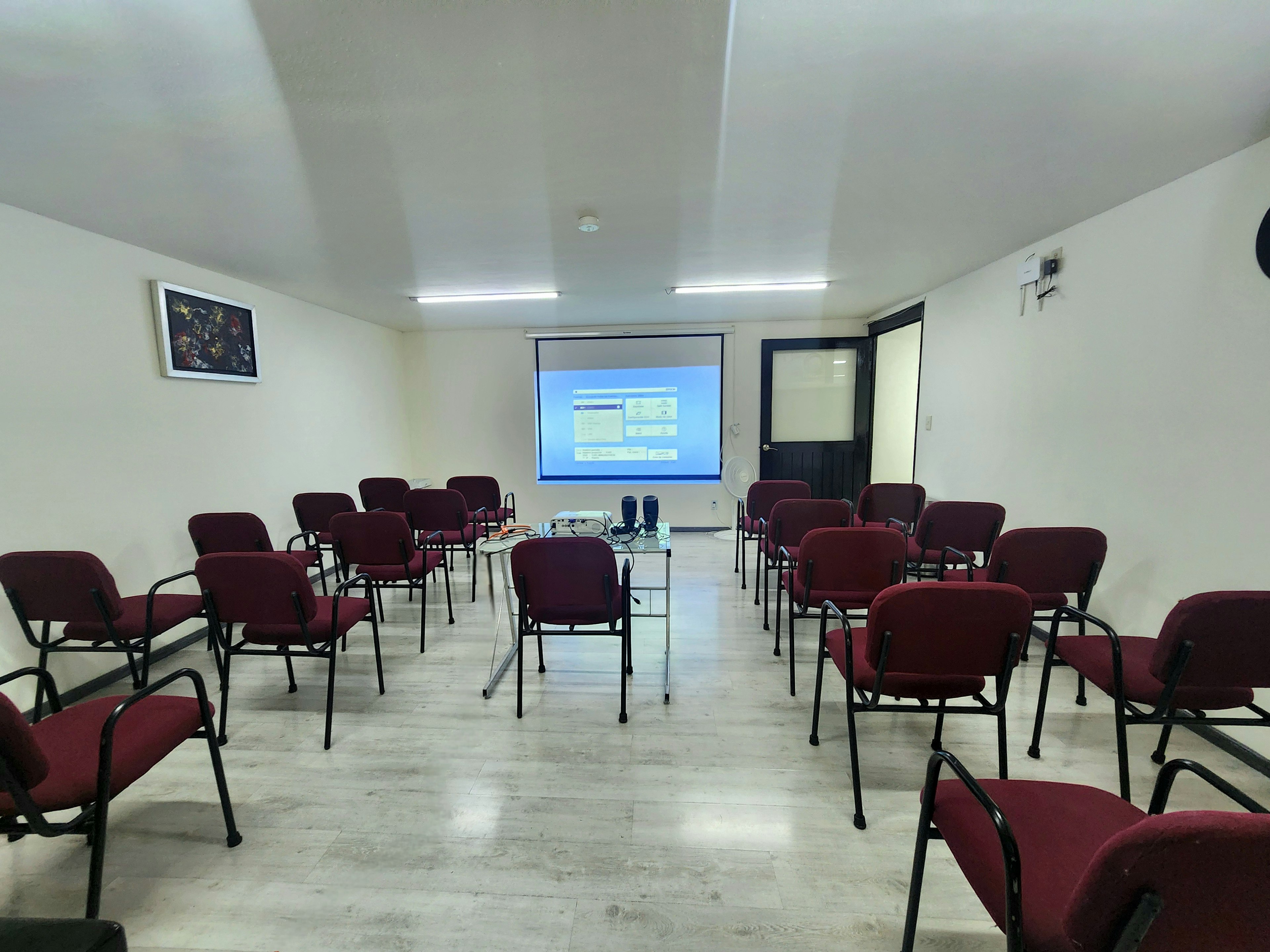 Sala de conferencias moderna y espaciosa con sillas rojas alineadas frente a una pantalla de proyección. Ideal para presentaciones y reuniones empresariales.