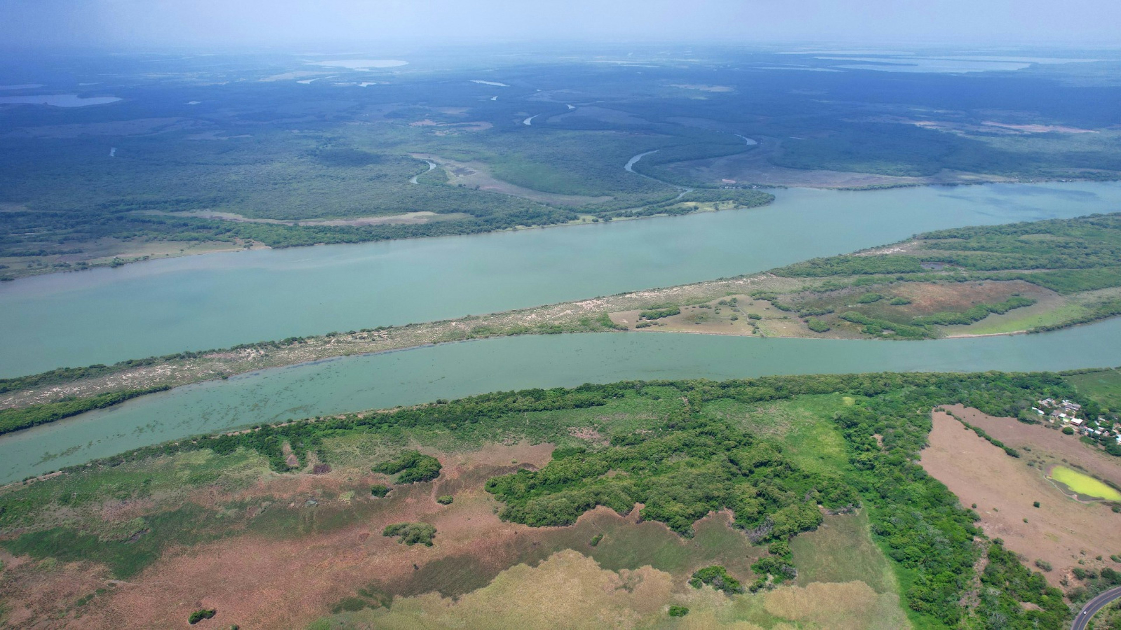 La imagen muestra una vista aérea de un extenso paisaje fluvial con un amplio río serpenteante rodeado de vegetación verde y algunas áreas de tierra despejada. Esta vista panorámica podría ser atractiva para desarrollos inmobiliarios de lujo con vistas al agua, resorts ecoturísticos o propiedades residenciales exclusivas que aprovechen la belleza natural y el acceso al agua.