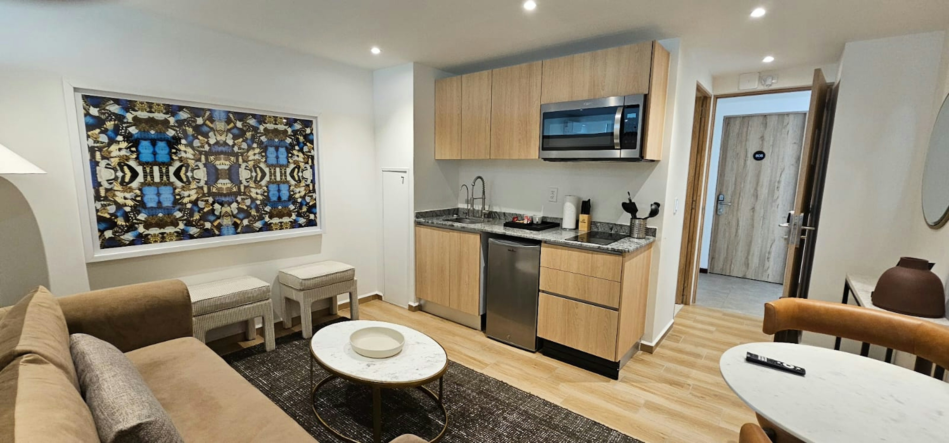 Interior moderno de un apartamento con cocina integrada. Muebles de madera clara y electrodomésticos de acero inoxidable. Sala de estar con sofá y mesa redonda. Decoración contemporánea.