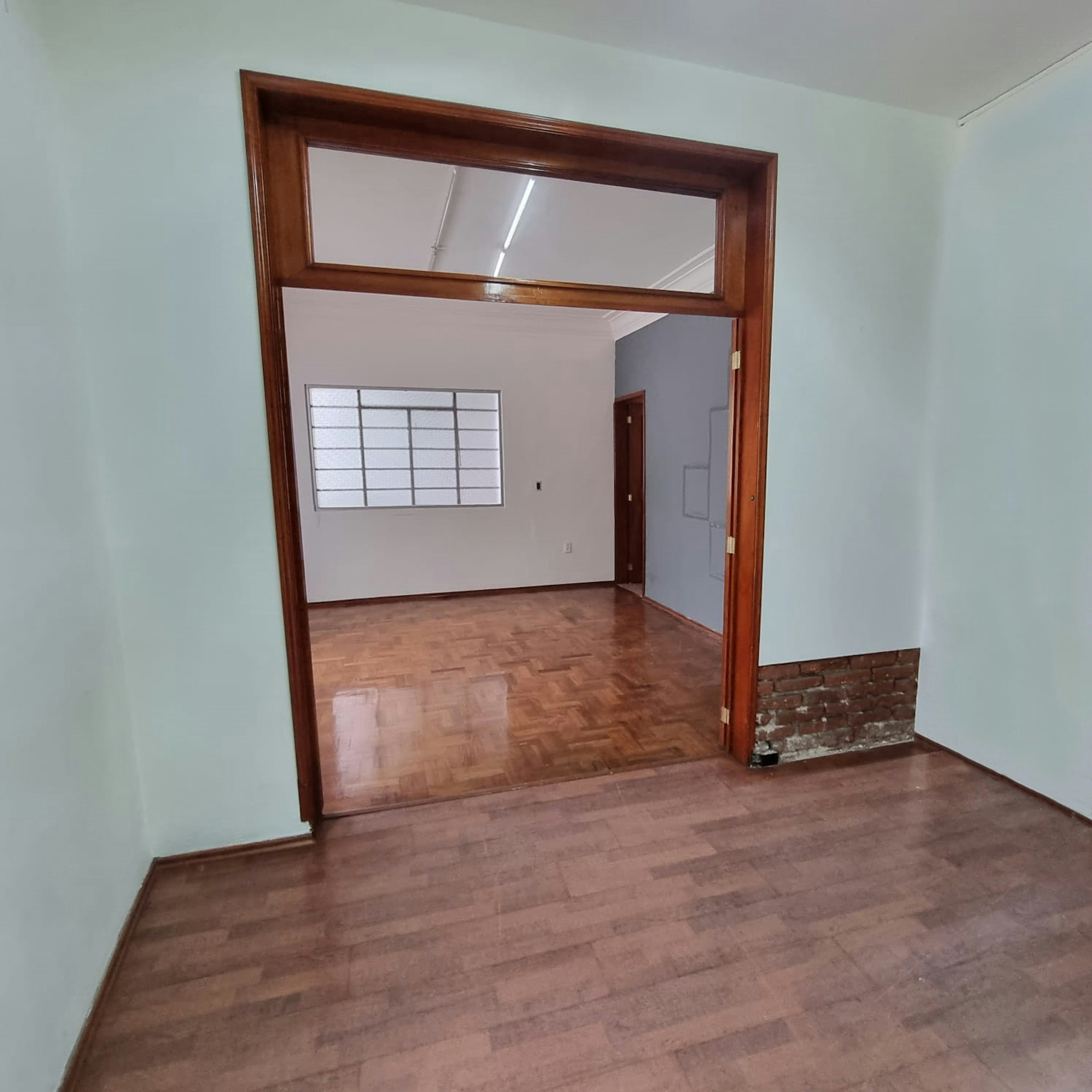 Espaciosa habitación interior con grandes puertas de madera y marcos, piso de parquet y una pared parcialmente expuesta de ladrillo. Iluminación natural a través de claraboyas en el techo.