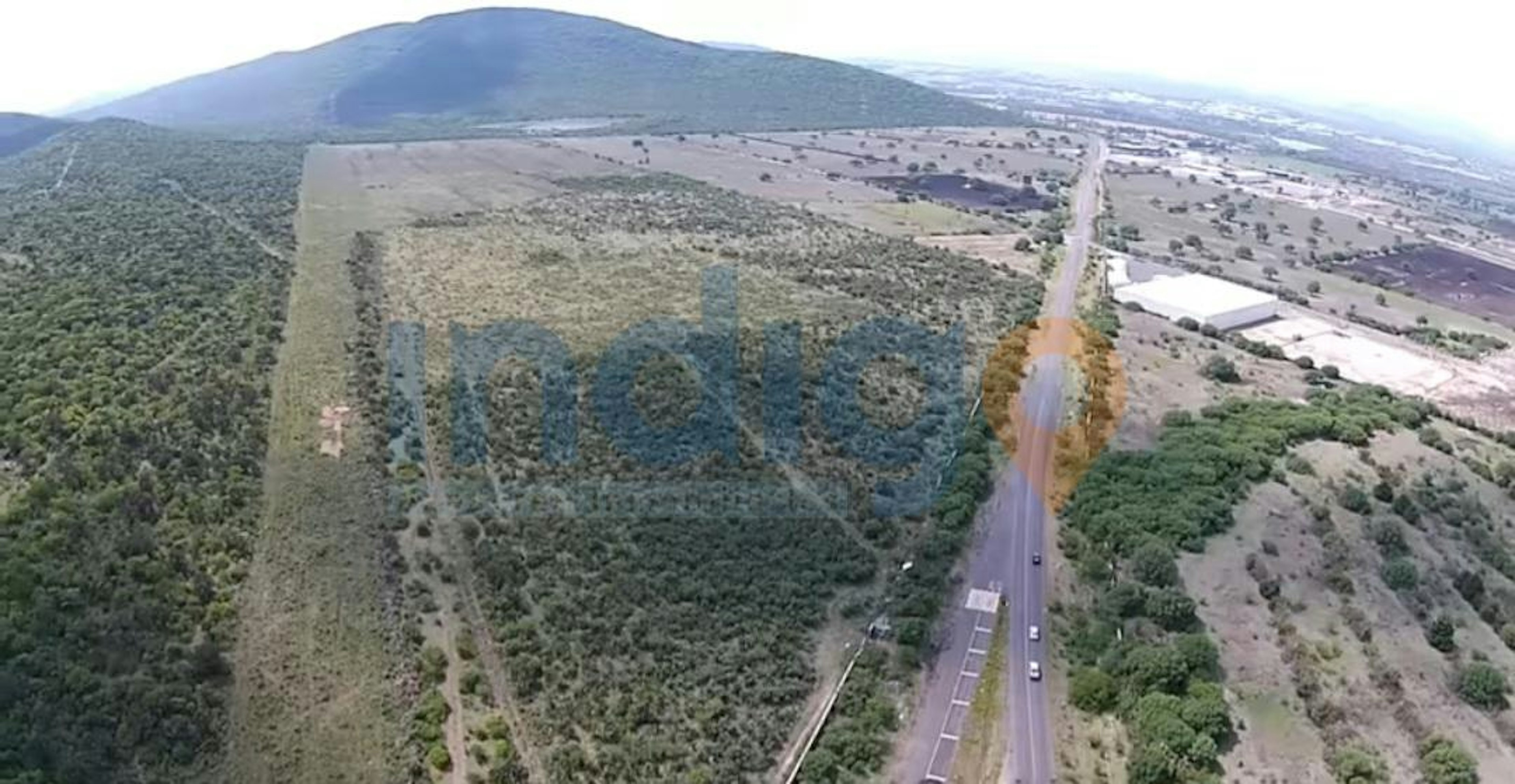 Vista aérea de un terreno extenso al lado de una carretera, ideal para desarrollo inmobiliario o agrícola. La imagen muestra una zona verde con potencial de crecimiento.