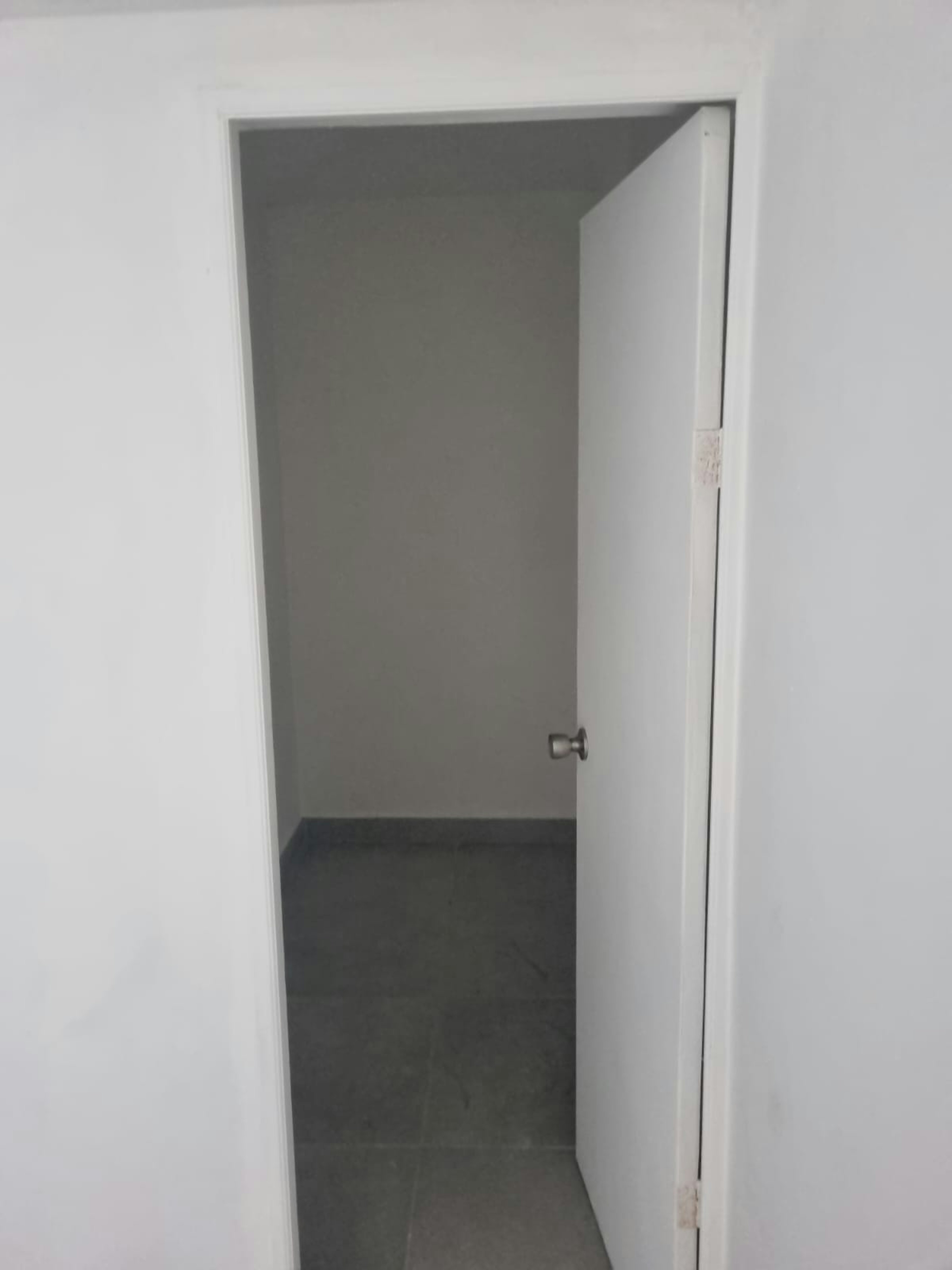 La imagen muestra una puerta abierta que conduce a una habitación vacía con paredes grises y suelo de baldosas. La sencillez del espacio sugiere un lienzo en blanco para posibles compradores o inquilinos.