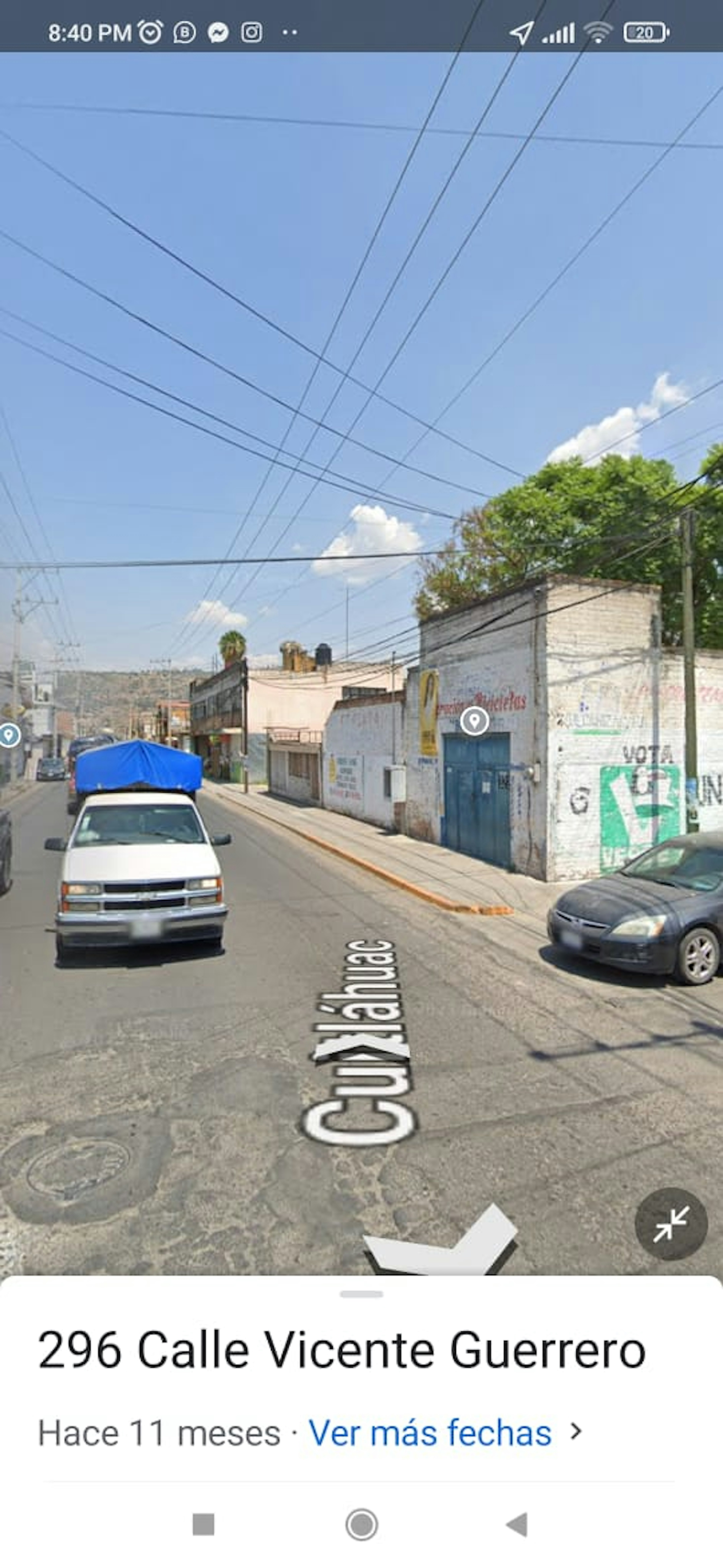 La imagen muestra una calle urbana con edificios de baja altura y muros pintados. Se ven cables eléctricos cruzando el cielo y varios vehículos estacionados. La calle parece estar en una zona residencial o comercial de baja densidad. El estado de los edificios y la infraestructura sugiere que podría ser un área en desarrollo o con potencial para renovación urbana.