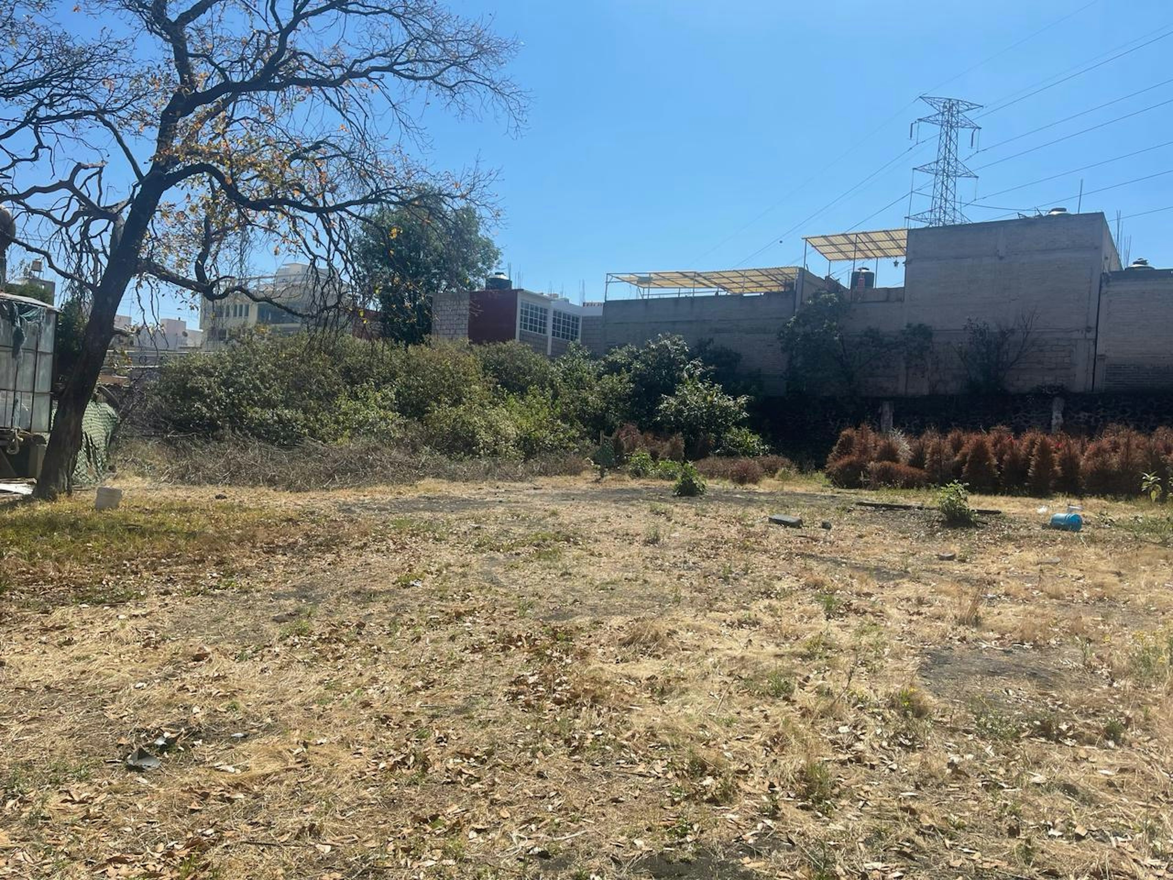 Terreno urbano desocupado, con vegetación dispersa y escombros. Potencial para desarrollo inmobiliario, rodeado de edificaciones y con acceso a servicios.