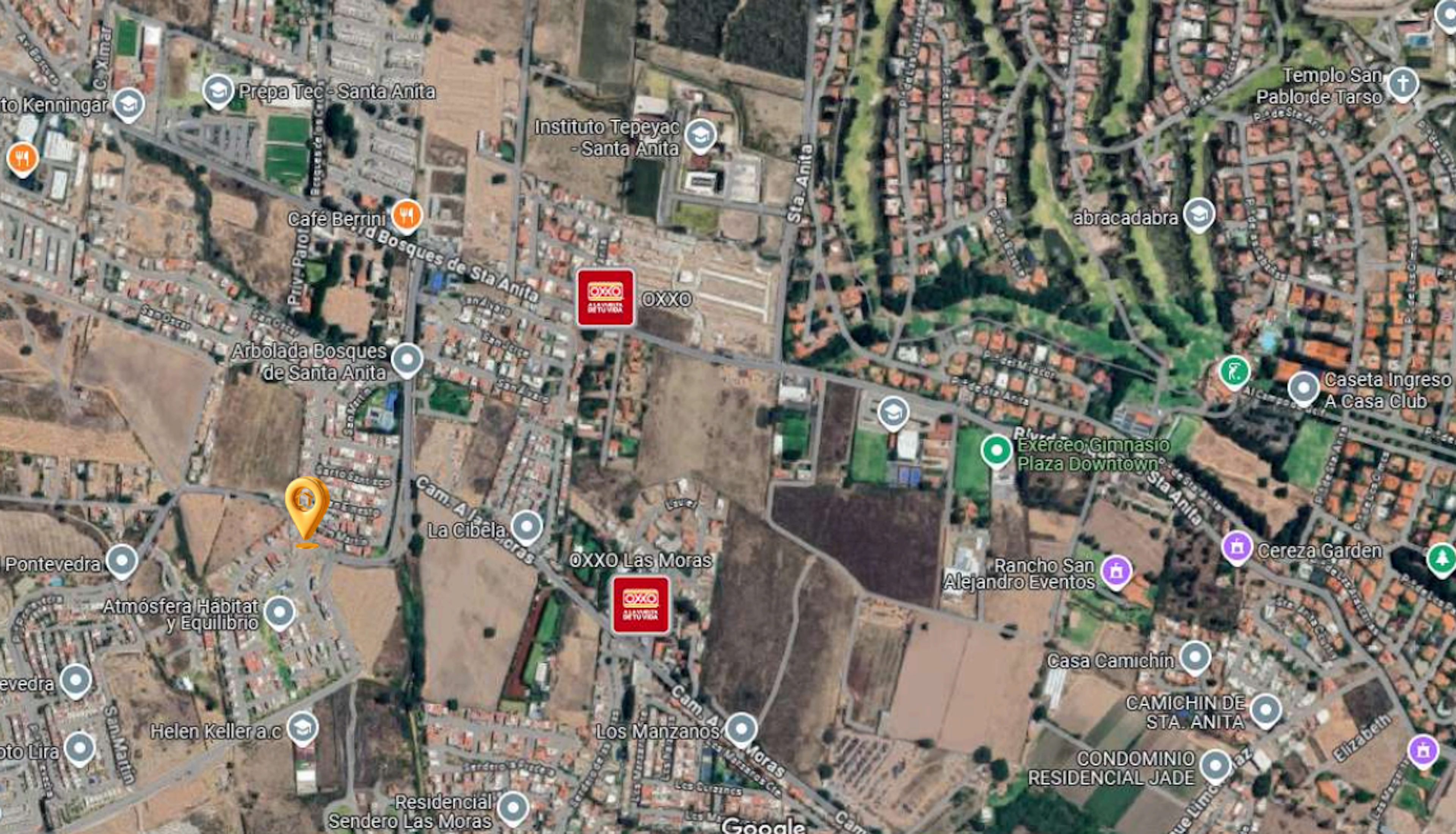 La imagen muestra una vista aérea satelital de una zona urbana en desarrollo, con áreas residenciales, instituciones educativas y espacios comerciales. Se observan terrenos sin construir junto a áreas densamente pobladas, evidenciando un crecimiento urbano en proceso. La presencia de tiendas OXXO y otros negocios sugiere una zona con servicios en expansión, ideal para inversiones inmobiliarias.