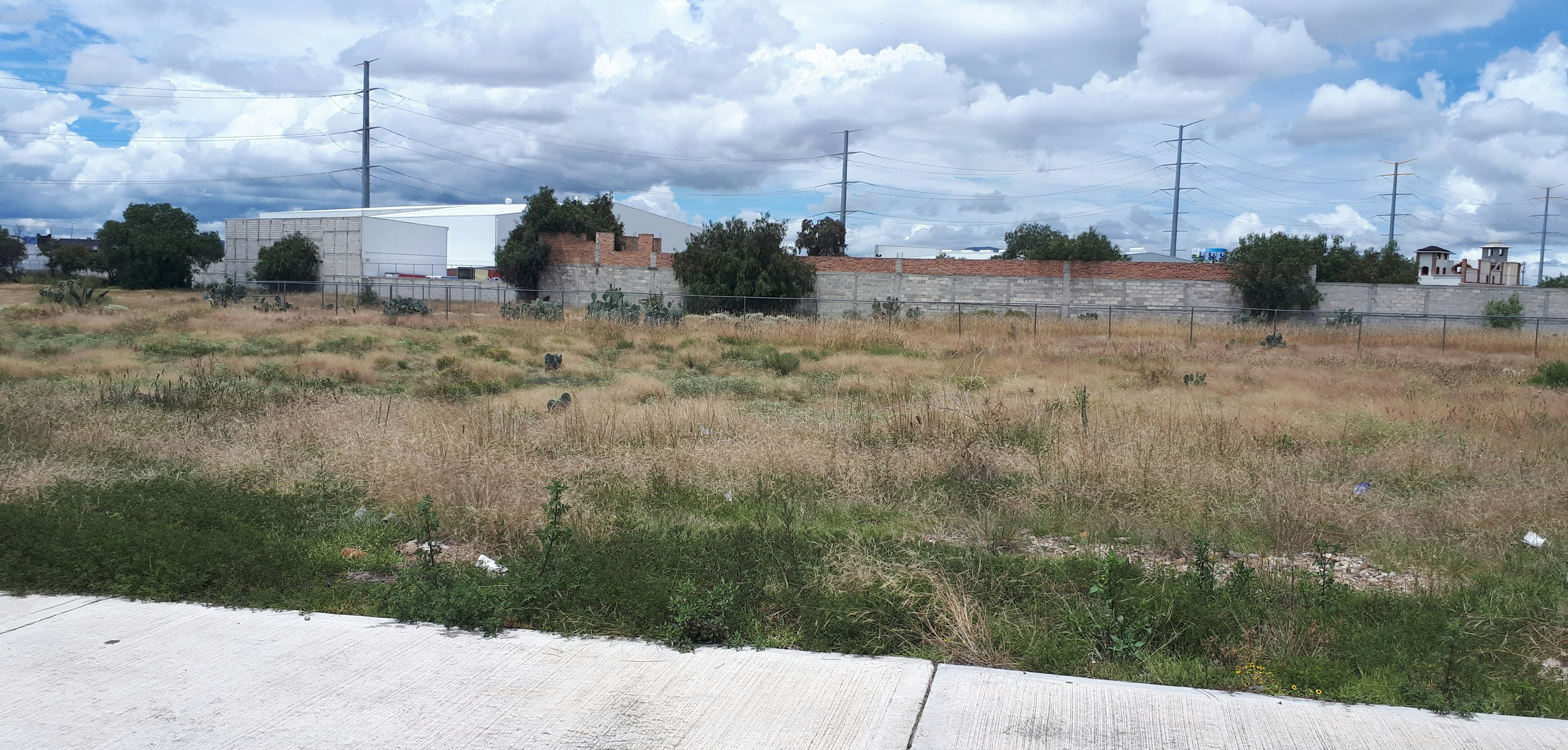 Terreno amplio y despejado en zona urbana, con vegetación baja y cercado parcial. Ideal para desarrollo inmobiliario o comercial, con acceso a servicios y vías principales.