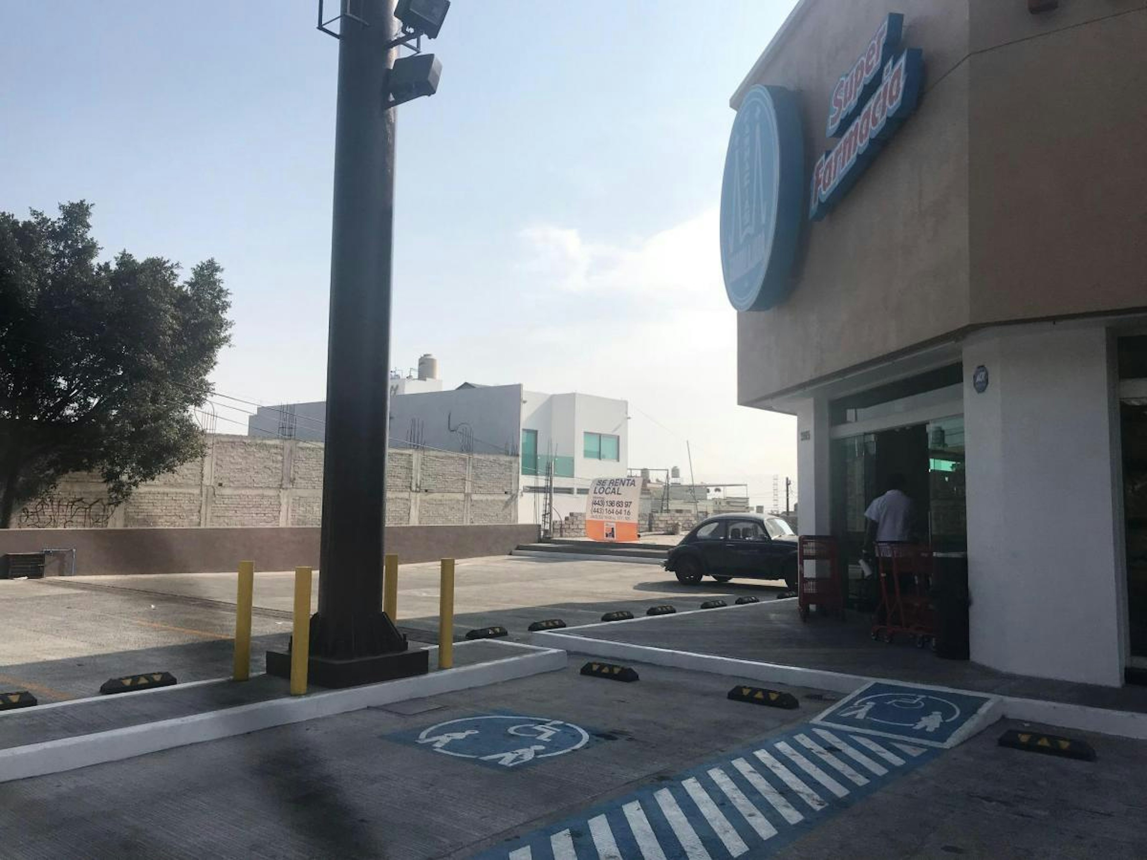 La imagen muestra un estacionamiento de un establecimiento comercial, posiblemente un supermercado, con señalizaciones de estacionamiento para discapacitados y una entrada accesible.