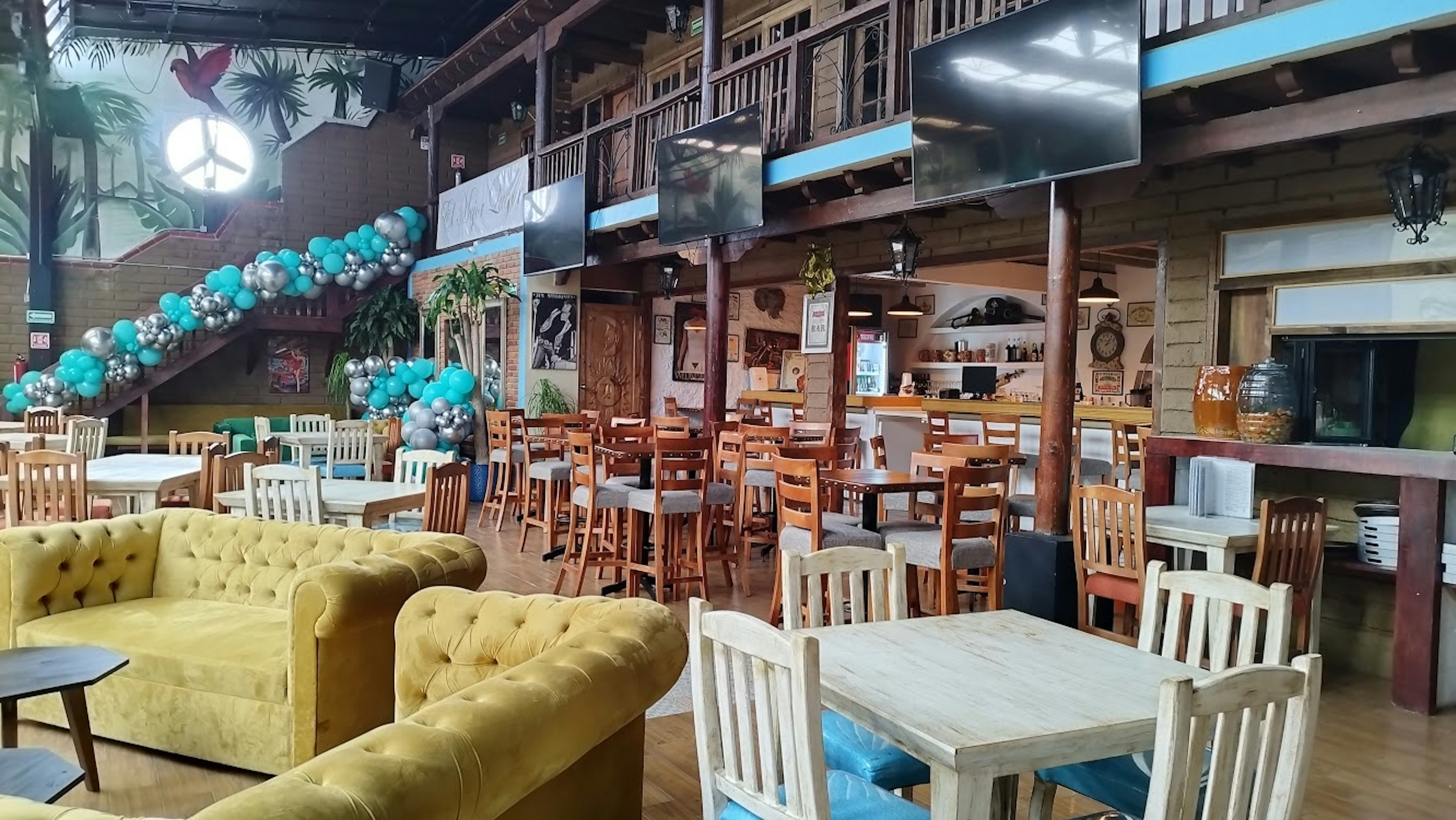 Espacioso restaurante con decoración rústica y mobiliario de madera. Cuenta con una zona de sofás, mesas y sillas para comensales, y una barra de bar.