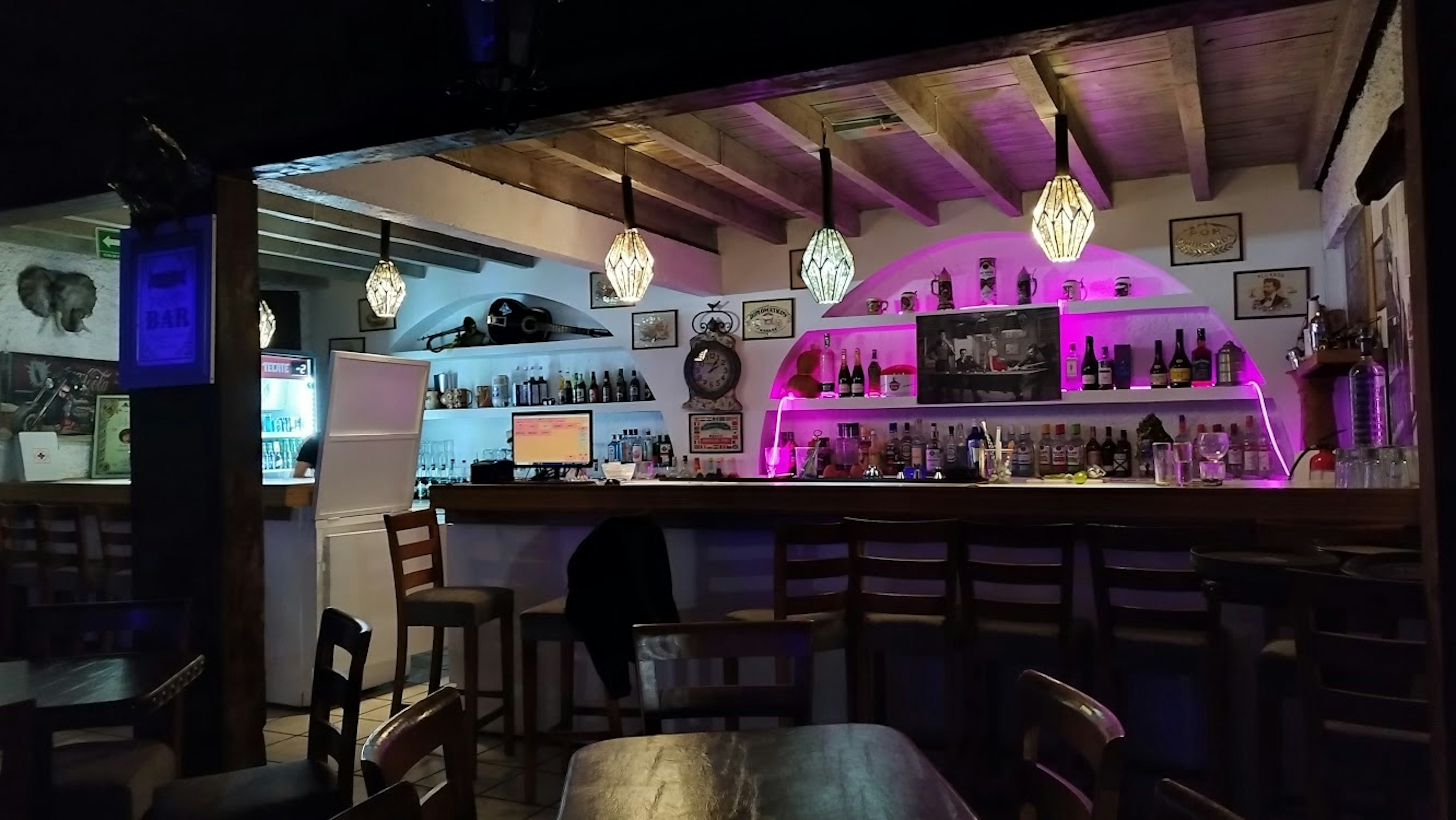 Interior de un establecimiento con barra de bar iluminada, sillas altas y decoración rústica. Ideal para negocio de hostelería.