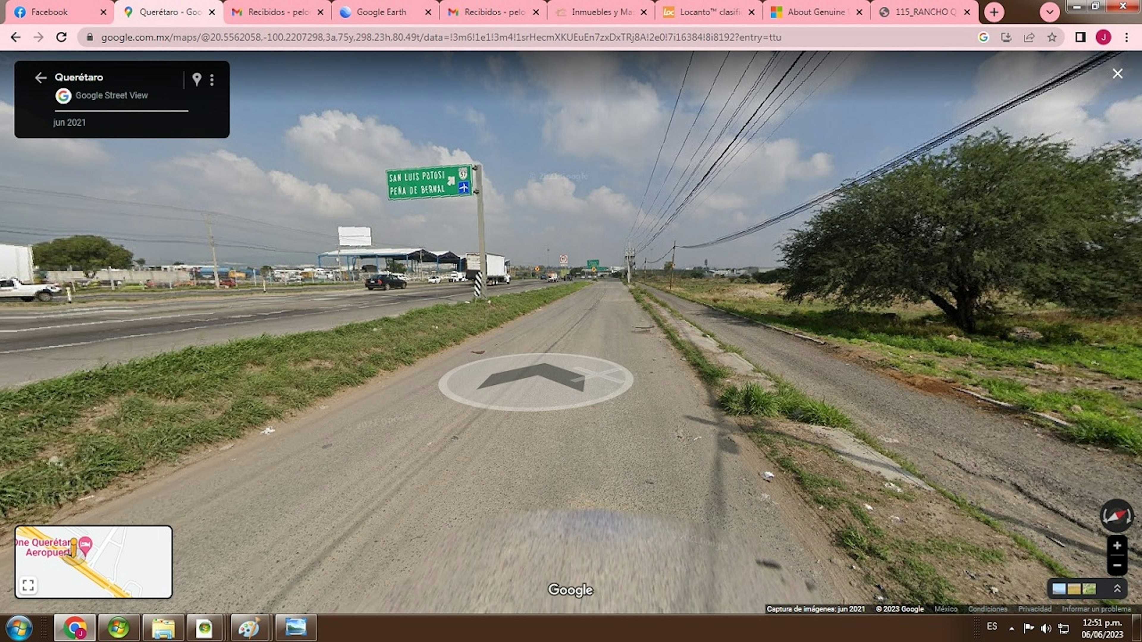 La imagen muestra una carretera en una zona semiurbana de México. Se ve un camino de tierra junto a una carretera principal, con vegetación y árboles alrededor. Hay señales de tráfico que indican direcciones hacia San Luis Potosí. Se observan líneas eléctricas y algunos edificios industriales en la distancia. El área parece tener potencial para desarrollo inmobiliario, con espacio disponible para construcción.