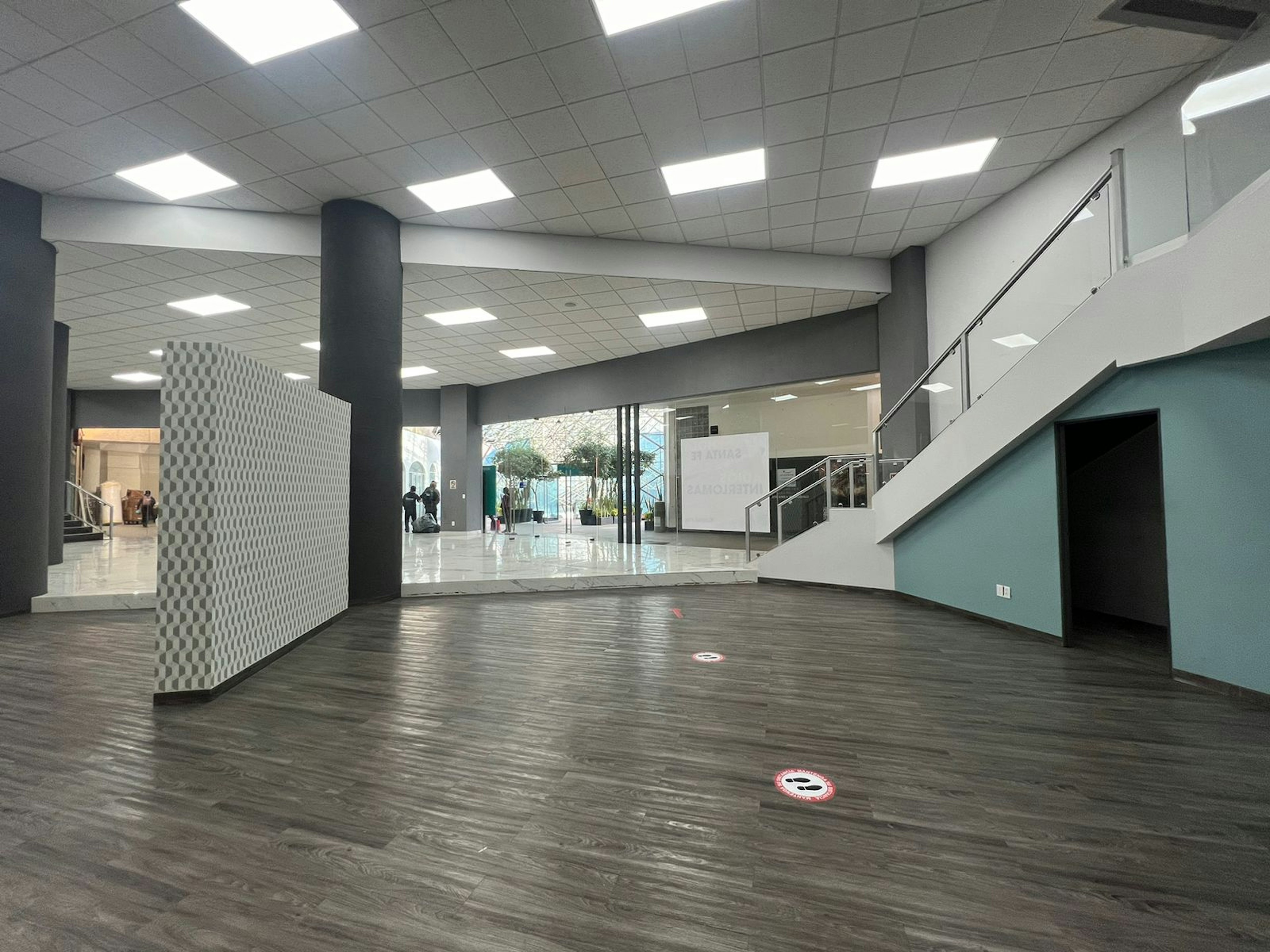 Espacioso vestíbulo de entrada en un edificio comercial con suelo de madera laminada, columnas modernas y escalera que conduce al segundo piso.