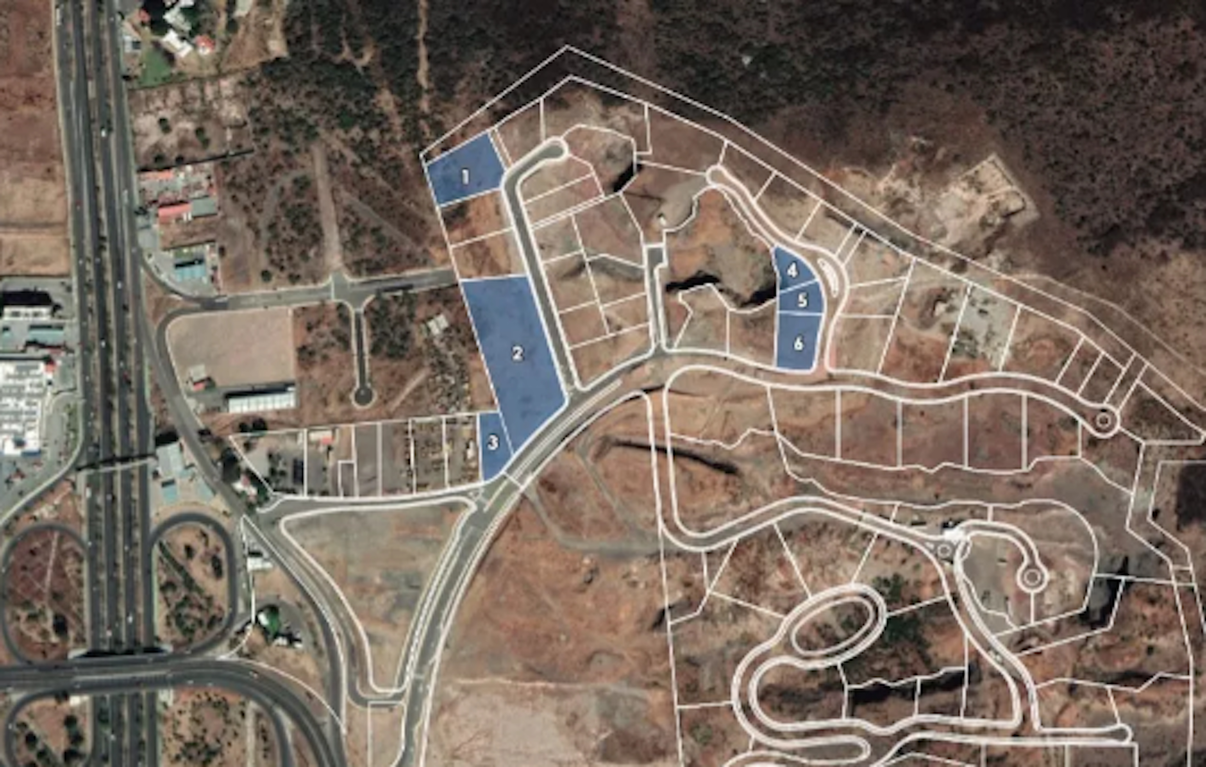 The image shows an aerial view of a developing residential area or planned community. It features a layout with numbered lots, roads, and infrastructure. The area appears to be in a semi-arid region with sparse vegetation. Blue-shaded sections likely indicate available or special lots. The surrounding landscape is undeveloped, suggesting a new suburban expansion on previously unused land.