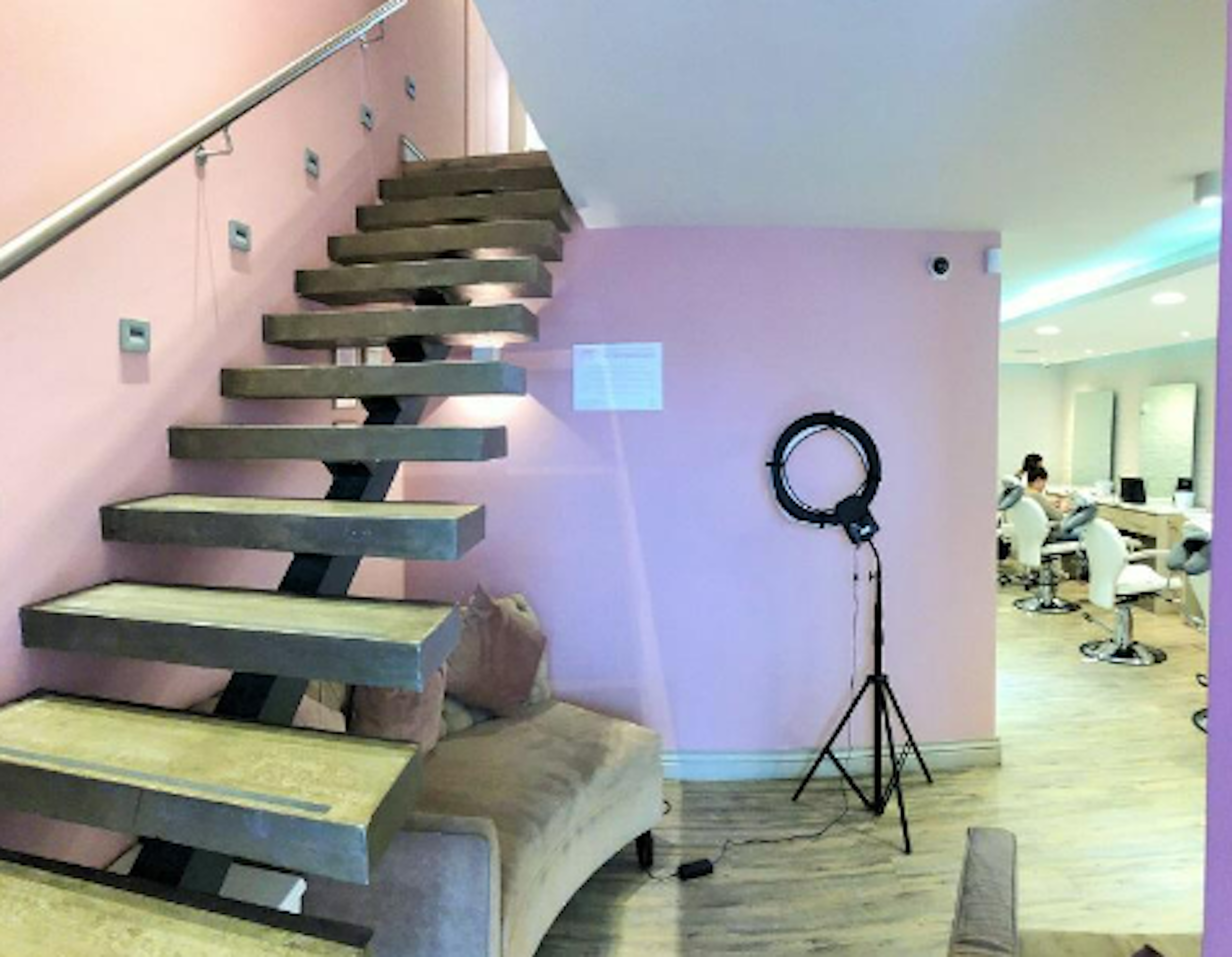 Interior moderno con escaleras flotantes de madera y metal, paredes rosadas y un área de salón al fondo. Iluminación suave y decoración minimalista.