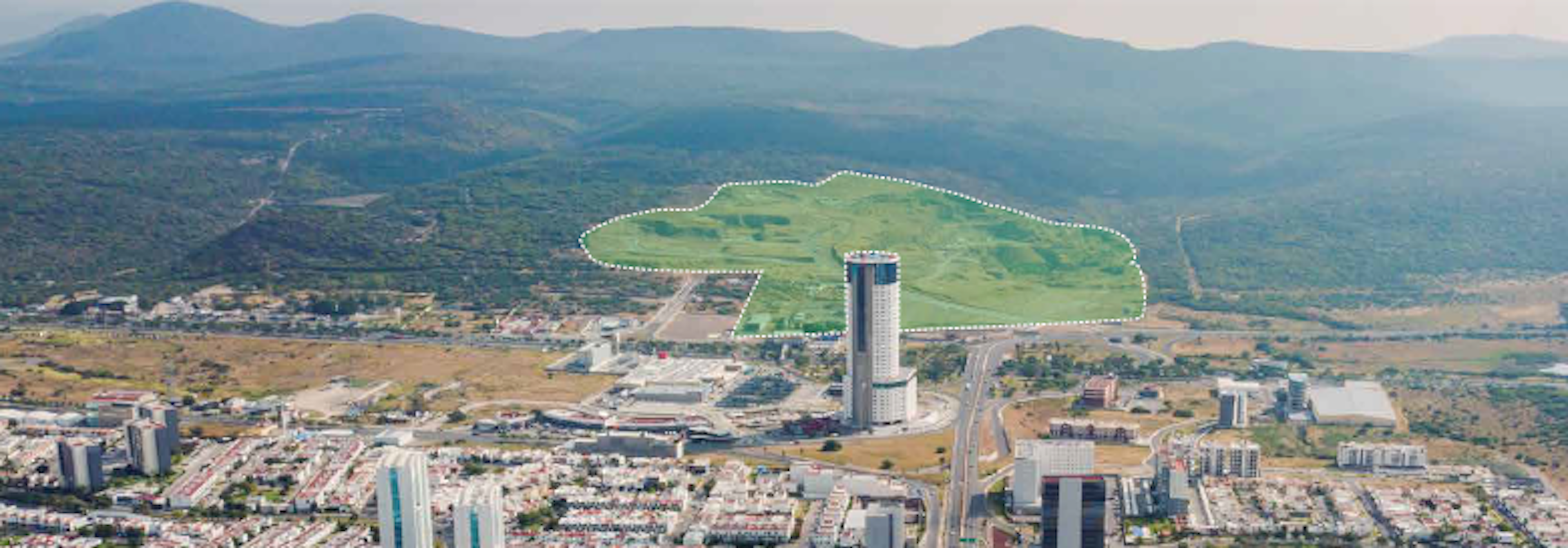 Vista aérea de un desarrollo inmobiliario que muestra una mezcla de edificios residenciales y comerciales con infraestructura moderna. Se observan carreteras y áreas verdes, con montañas en el fondo.