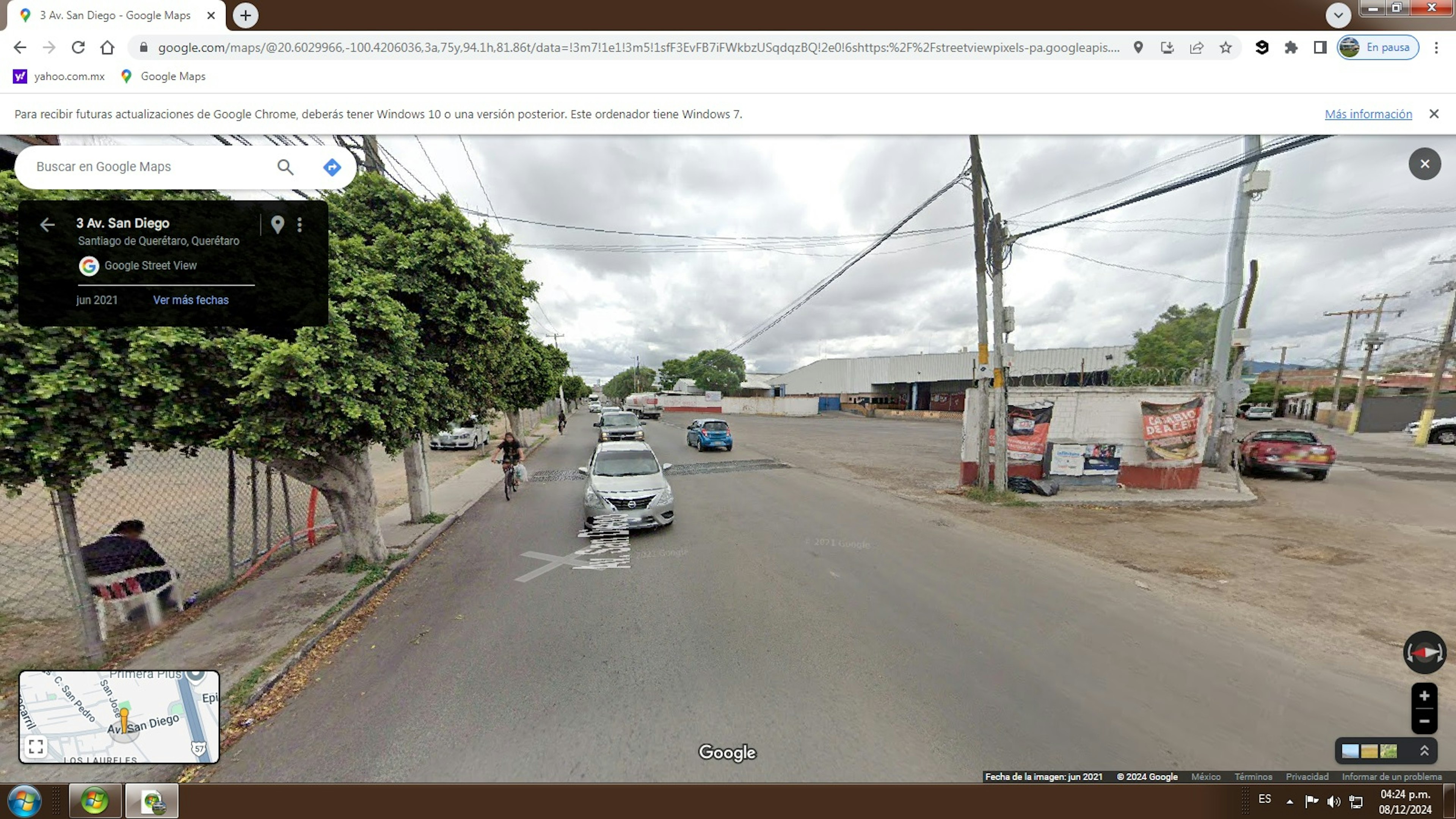 La imagen muestra una calle en Santiago de Querétaro, México, capturada por Google Street View. Se observa una avenida amplia con aceras, árboles y postes eléctricos. Hay varios vehículos estacionados y en circulación. Las construcciones visibles son principalmente muros y algunas estructuras comerciales. El área parece ser una zona mixta residencial y comercial, con potencial para desarrollo inmobiliario.