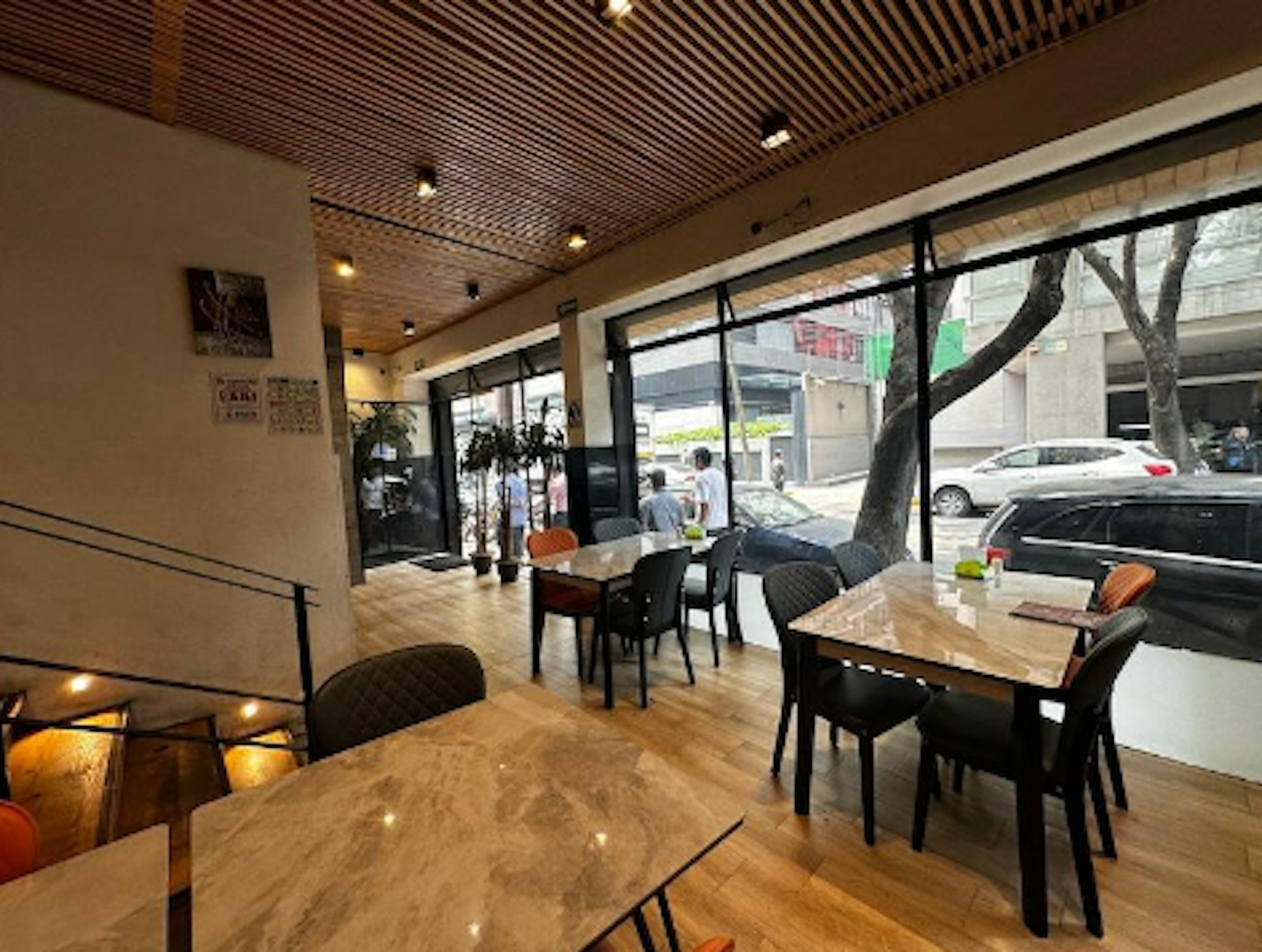 Espacioso local comercial con iluminación natural, acabados modernos y mobiliario elegante. Ideal para cafetería o restaurante, ubicado en zona urbana con amplios ventanales y diseño contemporáneo.