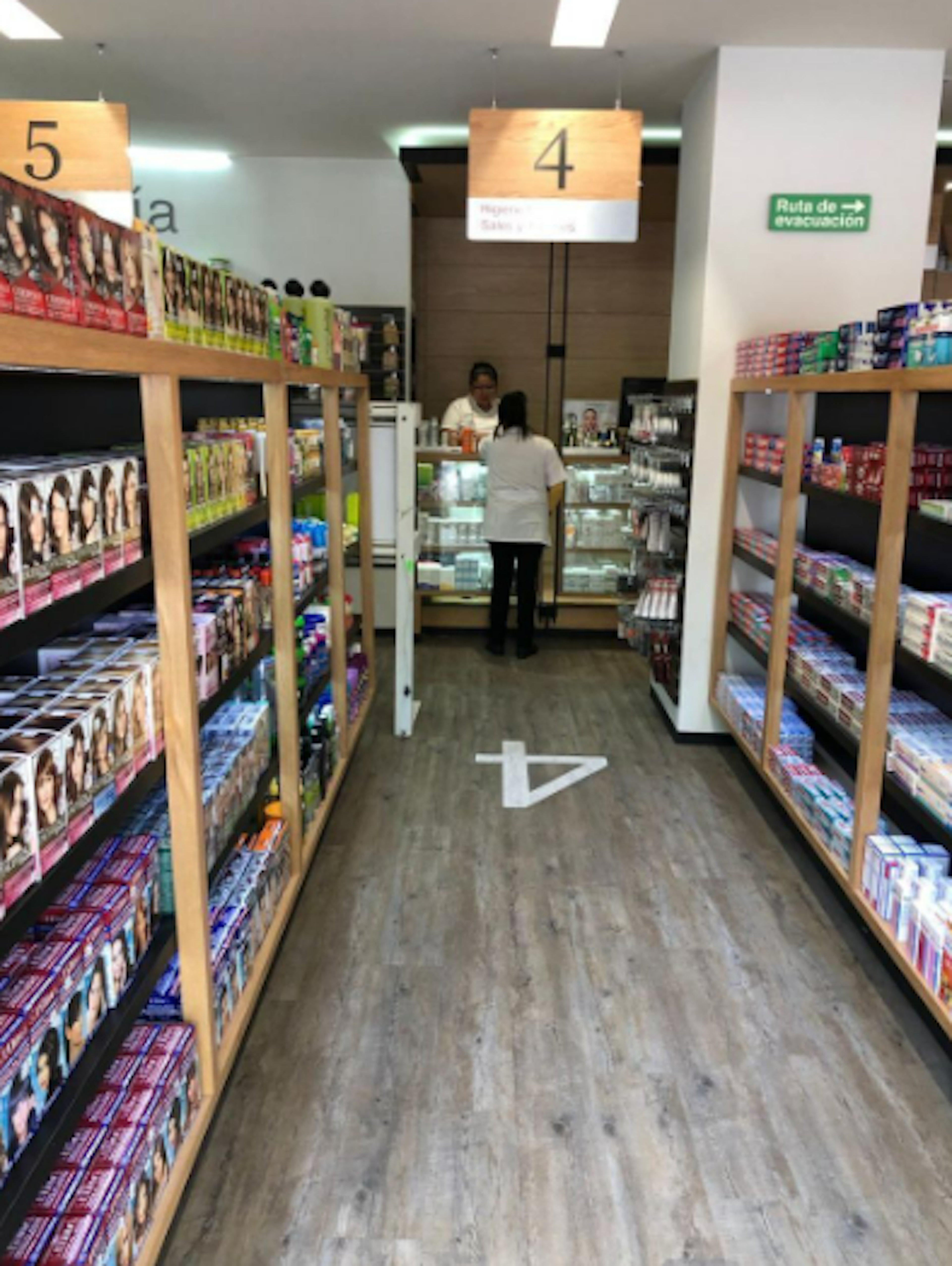 Interior de una tienda con estanterías de productos de belleza y cuidado personal. Se observa una señalización de ruta de evacuación y una persona al fondo.